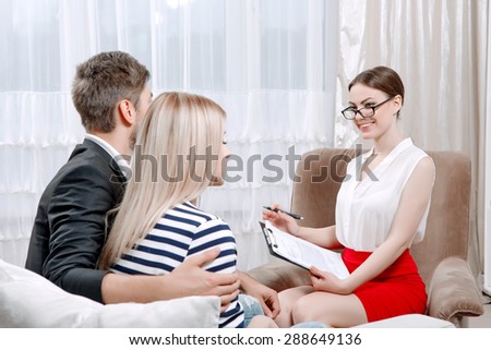Portrait of a professional female psychologist wearing white blouse and glasses, smiling to her clients young couple sitting cuddling in her office during therapy session, selective focus