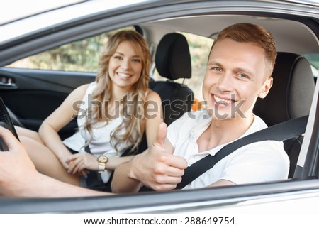 Sweet drive. Portrait of a handsome young man and beautiful blond girlfriend with curvy hair sitting in a white car smiling happily and showing thumbs up