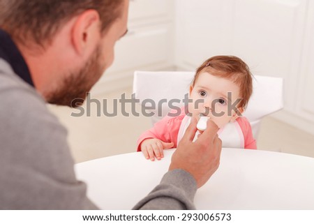Healthy eating. Nice little baby holding spoon in the mouth and looking at father while sitting on chair