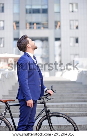 High goals.  Full length of nice bearded businessman  looking up and holding his bicycle while standing half turned.