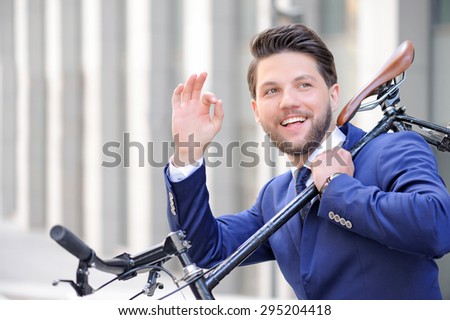 Everything is great. Nice smiling bearded businessman smiling and showing ok while holding bicycle on  his shoulders.