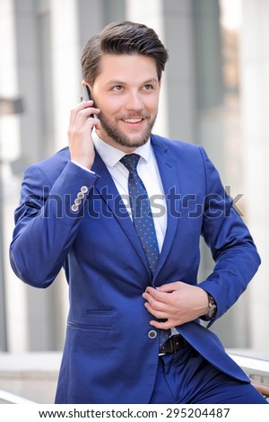 Be successful. Nice bearded businessman holding his hand on waist and smiling while talking on mobile phone.