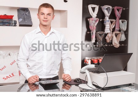 During work. Portrait of Serious handsome salesman standing near cash register in store.