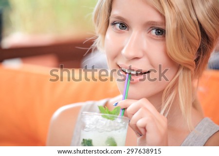 Refreshing drink. Beautiful young  smiling lady drinking cold cocktail in cafe.
