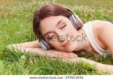 Relax and dream up. Nice beautiful girl  listening to music and lying on the grass while having nap.