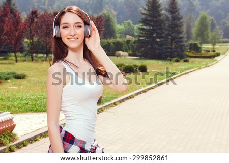 Best  way to reduce stress. Waist up of  upbeat nice young girl wearing headphones and listening music while walking in the park.