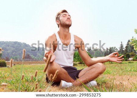 Finding inspiration in yoga. Nice positive guy sitting on the grass and closing his eye while relaxing.