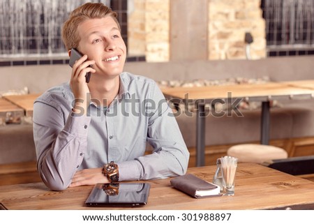 Pleasant conversation. Portrait of young-looking handsome man sitting in cafe and talking per mobile phone.