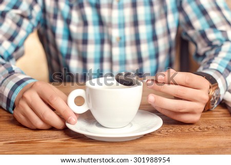 Coffee time. Close up portrait of young man having cup and tea spoon in cafe