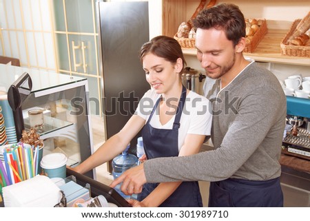 Supporting colleague. Male cafeteria worker showing to his female colleague how to use cash register