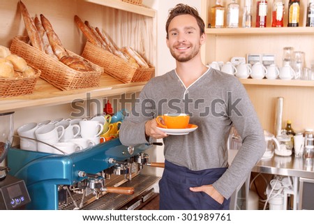 Do what you love. Young-looking handsome man posing with cup of coffee during his work in cafe