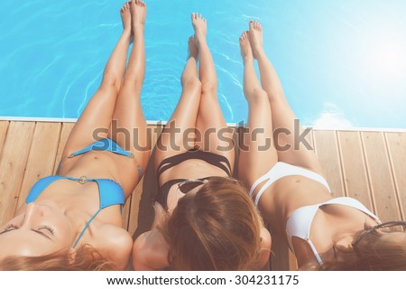 Pretty long legs. Top view of three beautiful ladies sitting at poolside stretching out their nice legs.