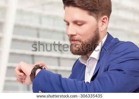 High time. Portrait of youthful handsome man with beard checking time on his new wristwatch