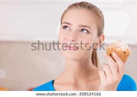 Food for thoughts. Nice charming vivacious girl holding muffin and keeping her glance up while mulling over in the kitchen