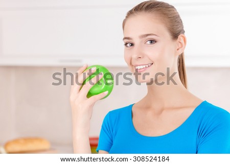 Apple a day keeps doctor away. Nice delighted young woman holding apple and showing positivity while standing in the kitchen.
