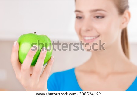 You are what you eat. Good looking contented pleasant girl holding apple and reveling in joy while standing in the kitchen