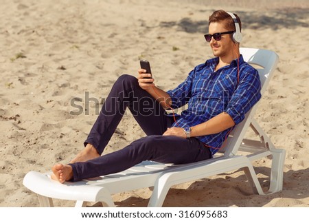 Feel the rhythm. Nice handsome delighted guy lying on the  sun bed and listening to music  while reveling in great time
