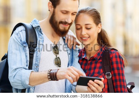 Lets have a look. Elated positive young couple standing together and holding mobile phone while expressing gladness