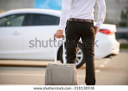 Just from abroad. Nice modern businessman going to his car and holding suitcase while evincing confidence.