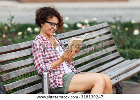 Gripping novel. Pretty upbeat positive girl holding book and reading it while relaxing on the bench