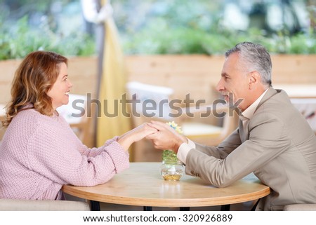 Elated feelings. Delighted blissful adult couple sitting at the table and holding hands of each other while evincing love
