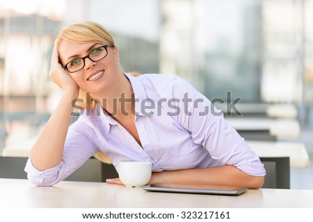 Time to relax. Cheerful upbeat charming businesswoman leaning on her hand and drinking tea while sitting at the table