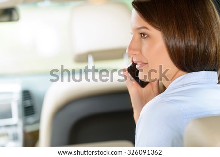 Modern way of life. Pleasant attractive content young girl holding mobile phone and having conversation while sitting in the car