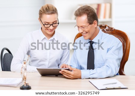 Look here. Vivacious positive professional lawyers sitting at the table and  holding laptop while surfing the Internet