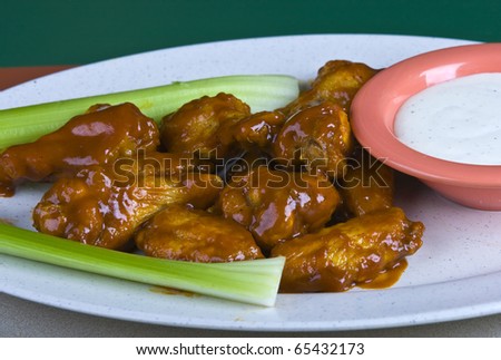 Buffalo chicken wings on plate with ranch dressing , and celery.
