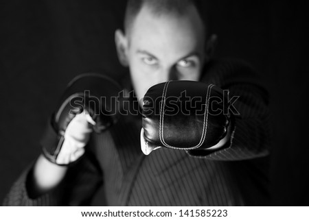 Business man dressed in business suite bunching in the direction of camera, focus at boxing glove.