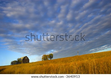 Farm building with spectacular sky during last moments of the sunset with sign saying “Little Hill Side Farm”on the background and prairie in the foreground