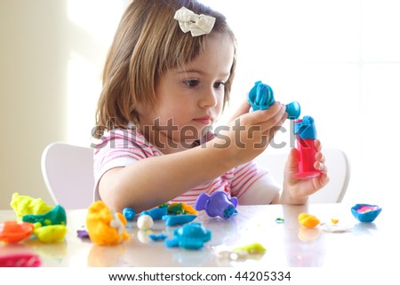 Little girl is learning to use colorful play dough in a well lit room near window