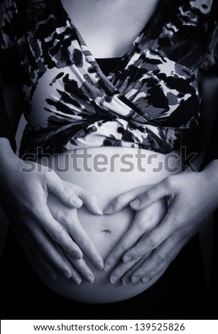Pregnant woman making heart shape with hands over her stomach