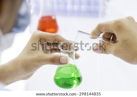 chemist purring blue liquid from flask to a green liquid beaker