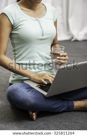 portrait of a young woman holding a glass of water in a sitting position while using her laptop