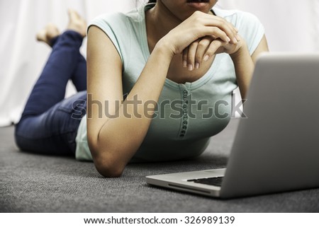 young woman laying on the floor and placing her hands on her chin while using her laptop
