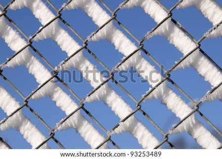 Snow on a wire fence against a blue sky.