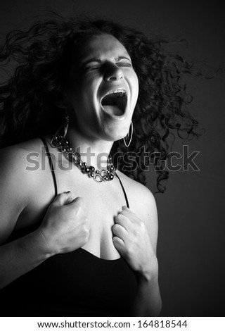 Toned black and white image of woman yelling with eyes closed.