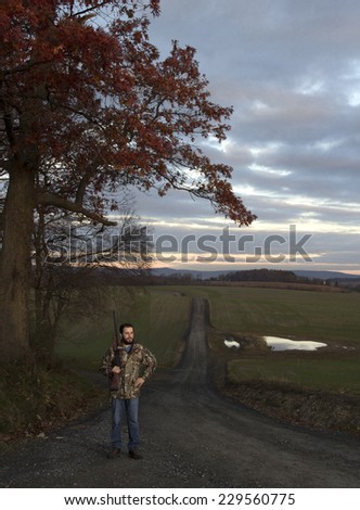 Man in road, carrying rifle at dawn.