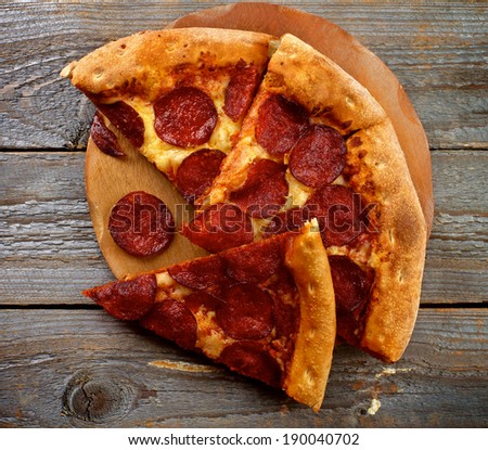 Tasty Pepperoni Pizza with Slice of Salami on Wooden Plate closeup on Rustic Wooden background. Top View