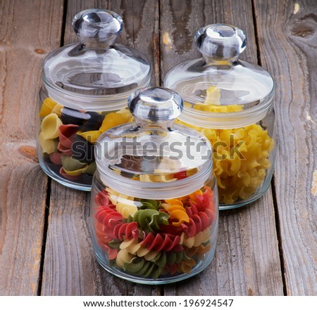 Three Glass Jars with Colorful Conchiglie Pasta, Ballerine Pasta and Rotini Pasta isolated on Wooden background