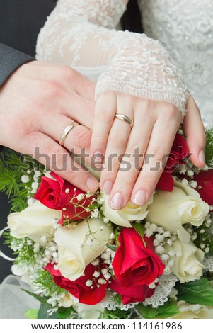 hands of the newlyweds with wedding rings on a bouquet of roses