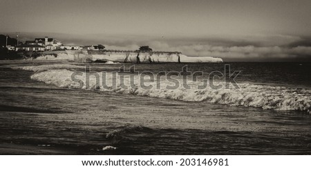 Black and white image of the Pacific Ocean coast and beach at sunset near the harbor in Santa Cruz, California, USA