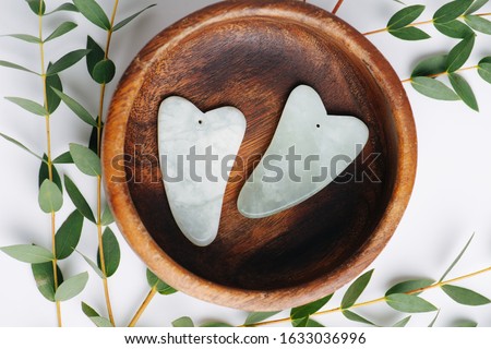 Chinese gua sha stones on a plate with eucalyptus branches over white. Top view. River jade shaped in a special way for a traditional chinese face massage. Foto stock © 