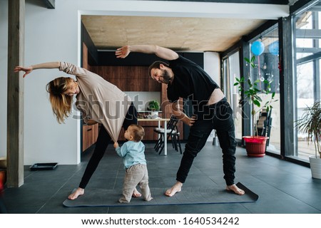 Family doing yoga. Mother and father doing side tilts as a part of their morning exercise, while their child pulling mother's shirt, seeking attention.
