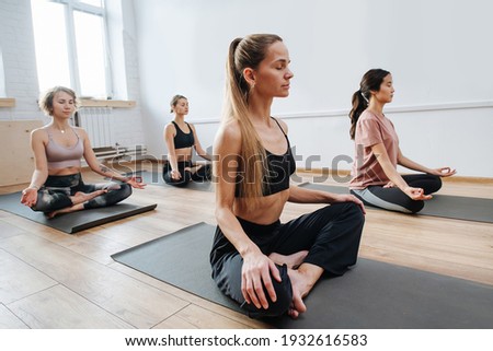 Peaceful young women practicing yoga in a group of four, sitting on a floor with legs closely tucked. Meditation, relaxing, clearing consciousness. Eyes closed, hands on knees.