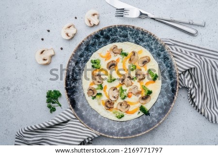 Omlette with mushrooms, paprika, broccoli on a plate. On a napkin on a table. Decorated with champignons halves and cutlery. Stock fotó © 