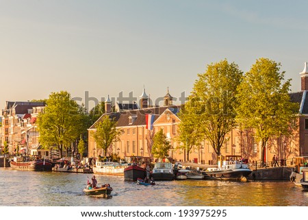 AMSTERDAM, THE NETHERLANDS - MAY 16, 2014: People relaxing on the Dutch Amstel river with the Hermitage museum situated in the background