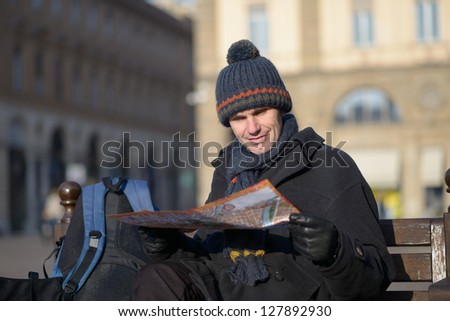 Tourist with city plan on a bench at winter