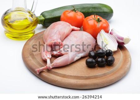 Raw rabbit legs with vegetables and olive oil on a wooden cutting board